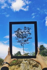 Close-up of hand holding frame against sky