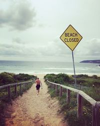 Shirtless man walking on pathway leading towards beach against sky