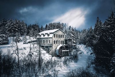 Bare trees by frozen house against sky during winter