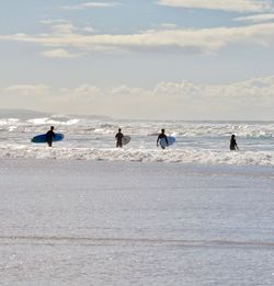 People with surfboards in sea against sky