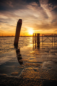 Wooden posts on beach against sky during sunset