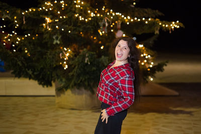 Portrait of smiling woman standing against illuminated christmas lights