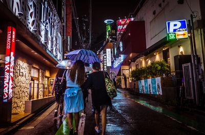 Rear view of people walking on wet street at night
