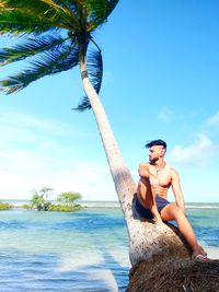 Full length of shirtless man on tree trunk by sea against sky