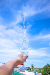 Midsection of person holding glass against blue sky