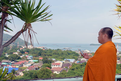 Side view of man wearing traditional clothing using smart phone while standing against sky