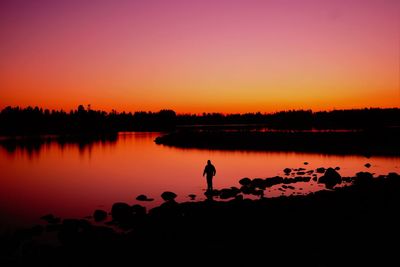 Silhouette man standing by lake against sky during sunset