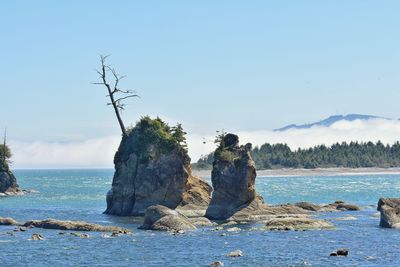 Scenic view of rocks by sea against clear blue sky