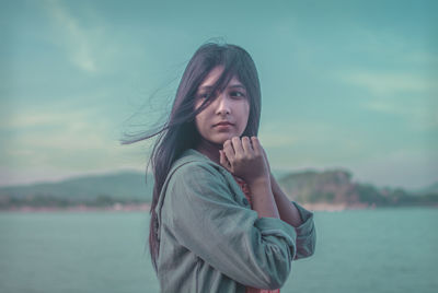 Portrait of young woman standing against lake