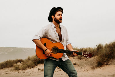 Young man holding guitar at beach