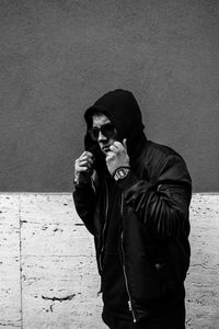 Hooded young man standing against wall