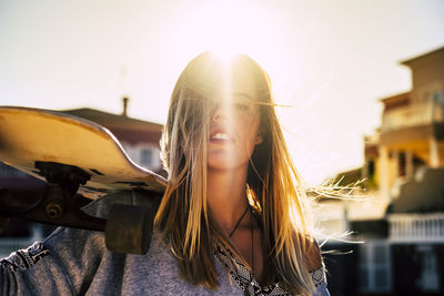 Close-up portrait of young woman with skateboard in city on sunny day