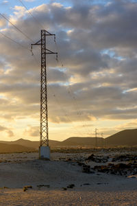 Electricity pylon on land against sky during sunset