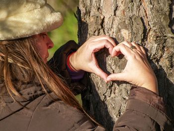 Mature woman making heart shape on tree trunk