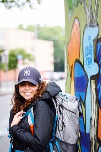 Portrait of smiling young woman standing by graffiti wall