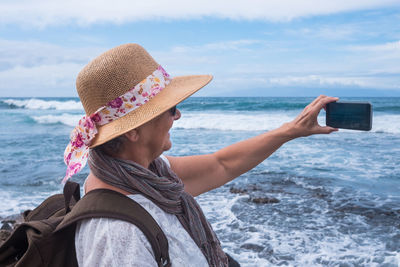 Happy senior woman clicking selfie while standing against sea