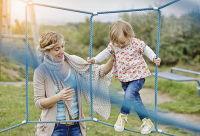 Girl on playground in climbing net supported by mother