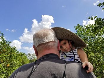 Grandfather carrying daughter against sky