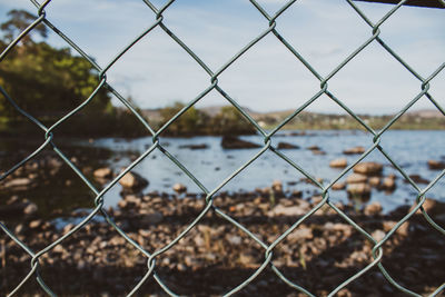 Close-up of chainlink fence against lake and sky in ireland 