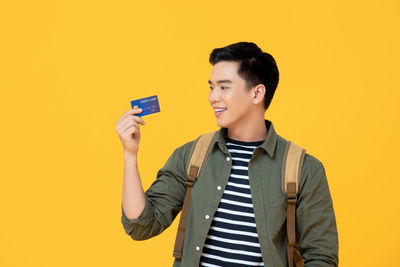 Young man looking away while standing against yellow background