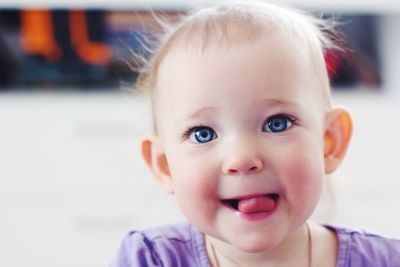 Close-up portrait of baby girl sticking out tongue at home