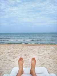 Low section of man relaxing on lounge chair at beach