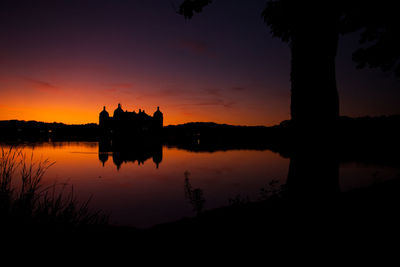 Silhouette built structure by lake against orange sky