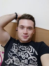 Portrait of young man standing against wall at home