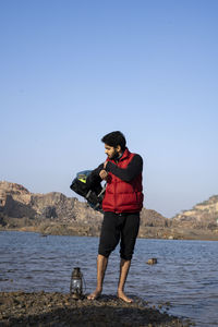 Young indian traveler getting ready for camping in the mountains, sitting near a lake 