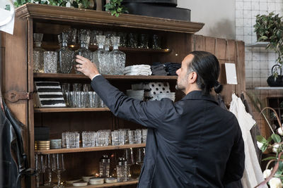 Rear view of mature man choosing glass container from shelf at store