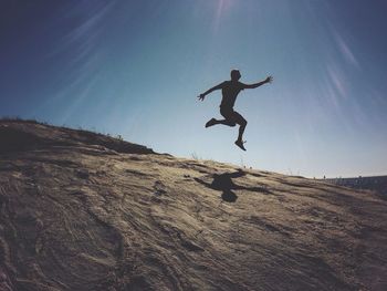 Low angle view of woman jumping against blue sky