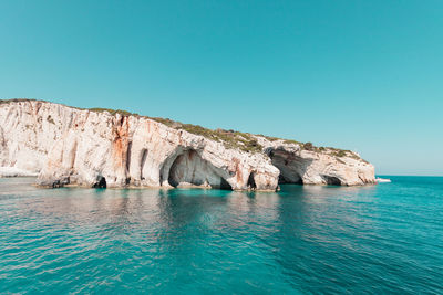 Rock formation in sea against clear blue sky