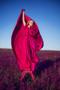  beautiful young woman on a pink stepladder in a pink dress in a field with wildflowers in summer