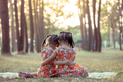 Rear view of sisters sitting in forest during sunset