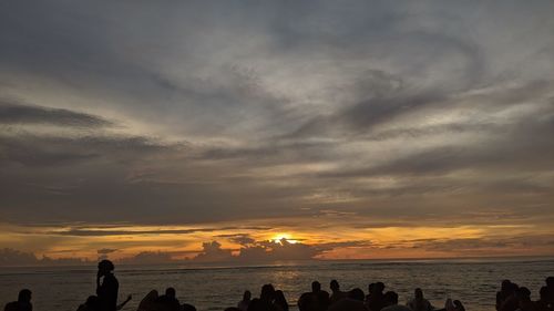 Silhouette people on beach against sky during sunset