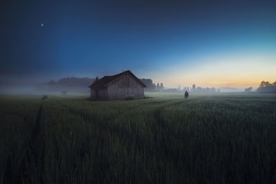 Man by hut on field against sky at dusk