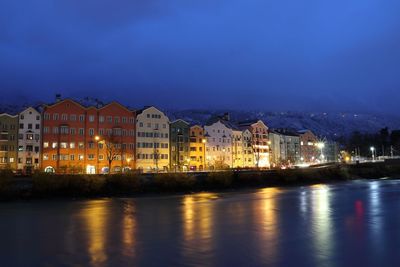 Illuminated buildings by river against sky at dusk