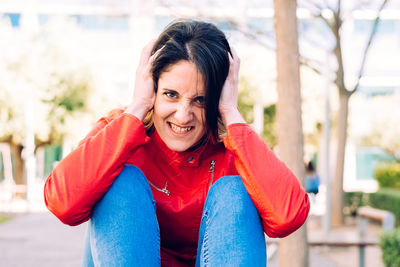 Portrait of angry woman covering ears while sitting outdoors