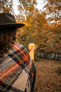 Rear view of woman holding coffee cup in forest during autumn
