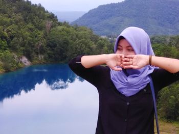 Young woman wearing hijab standing by lake against trees