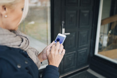 High angle view of woman unlocking house door through smart phone app