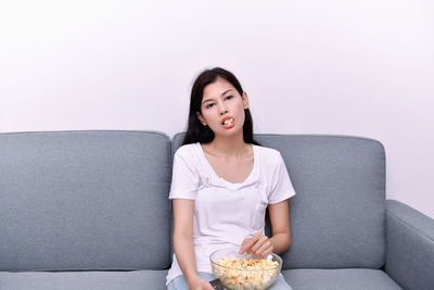 Portrait of woman eating popcorn while sitting on sofa at home