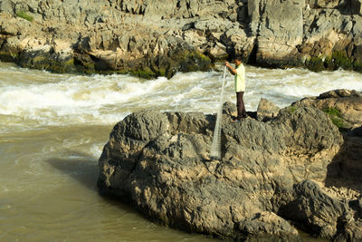 Side view of fisherman standing on cliff by river