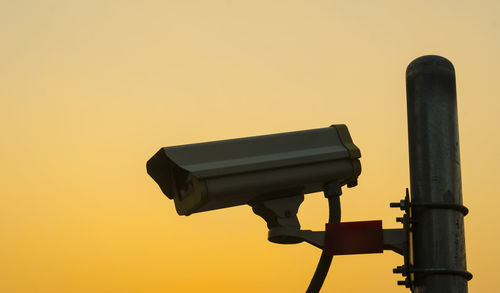 Low angle view of security camera against clear sky during sunset