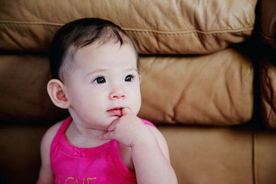 Close-up of cute baby girl with finger in mouth at home