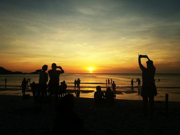 Silhouette people on beach against sky during sunset