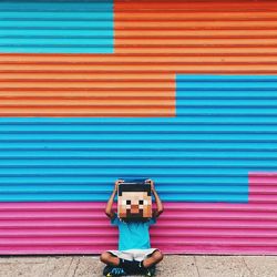 Obscured person sitting with cross-legged and mask against colorful store shutter