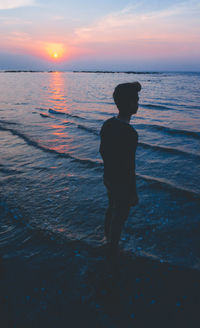 Rear view of silhouette man standing at beach during sunset