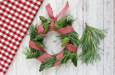 High angle view of homemade pinewreath decoration with pine cones and an with plaid ribbon on table