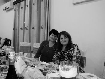 Portrait of mother-in-law and daughter sitting by dining table
